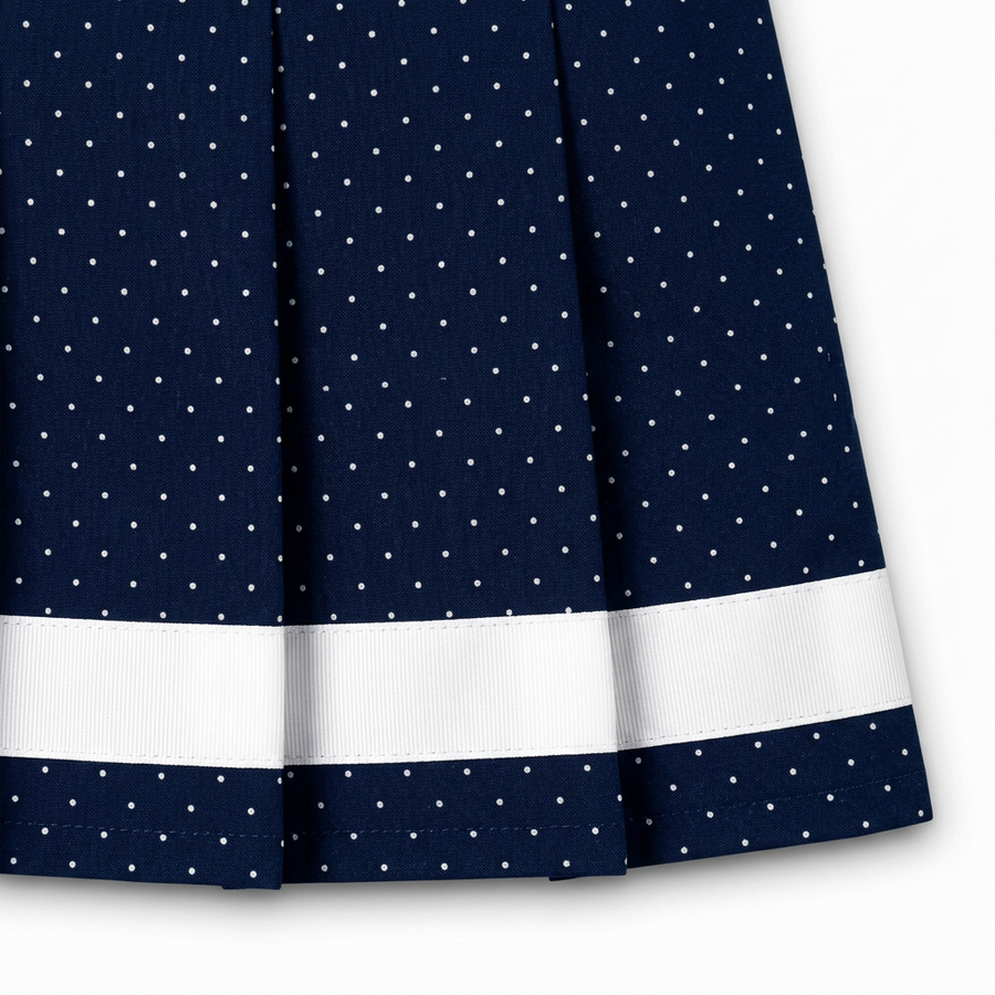 Close-up of Navy micro polka-dot pleats and white ribbon trim at the hem of the Renée skort.