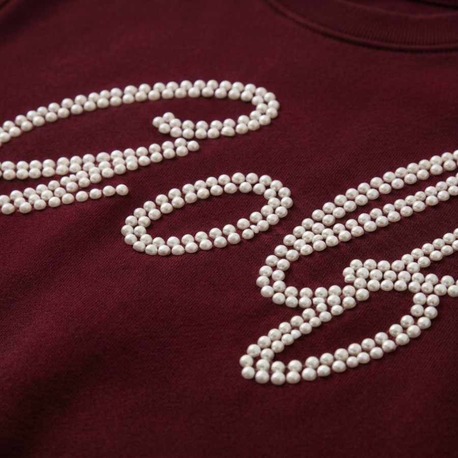 Close-up of white half pearls forming ‘Golf’ script on the merlot sweatshirt.