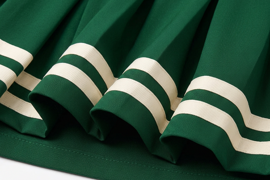 Close-up of twin ivory ribbon bands across the pleated hem of the green Charlotte skirt.